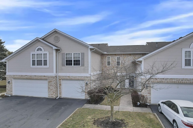 multi unit property featuring stone siding, an attached garage, and driveway