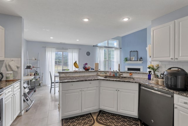 kitchen with a sink, stainless steel dishwasher, a peninsula, white cabinets, and decorative backsplash