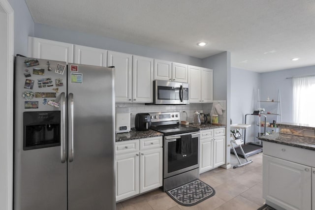 kitchen featuring light tile patterned floors, decorative backsplash, dark stone countertops, appliances with stainless steel finishes, and white cabinets