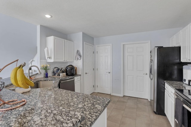 kitchen with dark stone countertops, a sink, appliances with stainless steel finishes, white cabinetry, and tasteful backsplash