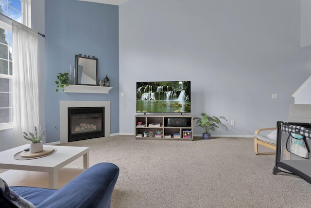 living area with carpet flooring, baseboards, a towering ceiling, and a fireplace