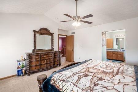 bedroom featuring visible vents, lofted ceiling, connected bathroom, carpet flooring, and baseboards