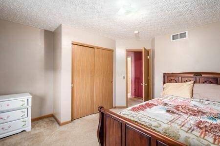 bedroom featuring visible vents, light colored carpet, a closet, and a textured ceiling