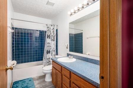 bathroom featuring visible vents, toilet, a textured ceiling, shower / tub combo, and vanity