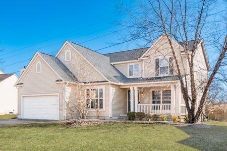 traditional-style house with a garage, covered porch, driveway, and a front yard