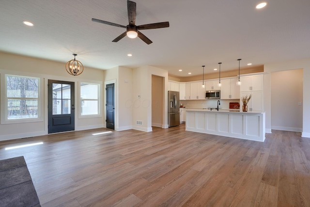 kitchen featuring light wood finished floors, open floor plan, light countertops, stainless steel appliances, and white cabinetry