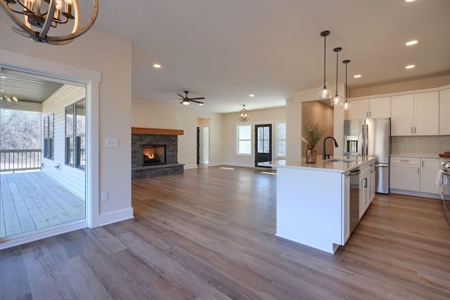 kitchen with backsplash, a stone fireplace, wood finished floors, stainless steel appliances, and a sink