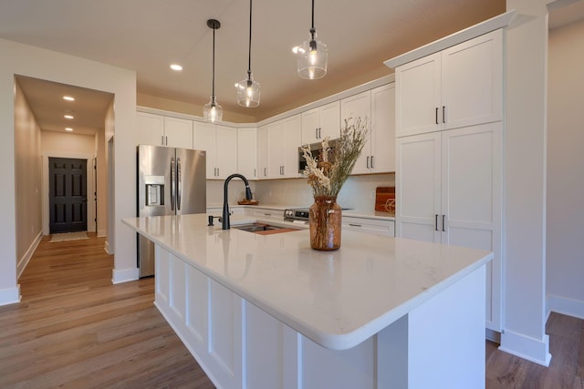 kitchen featuring light wood finished floors, an island with sink, stainless steel appliances, white cabinetry, and a sink