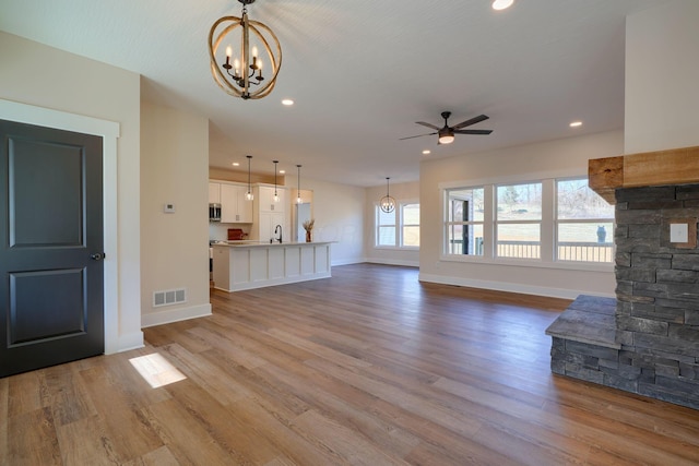 unfurnished living room with visible vents, ceiling fan with notable chandelier, wood finished floors, recessed lighting, and baseboards