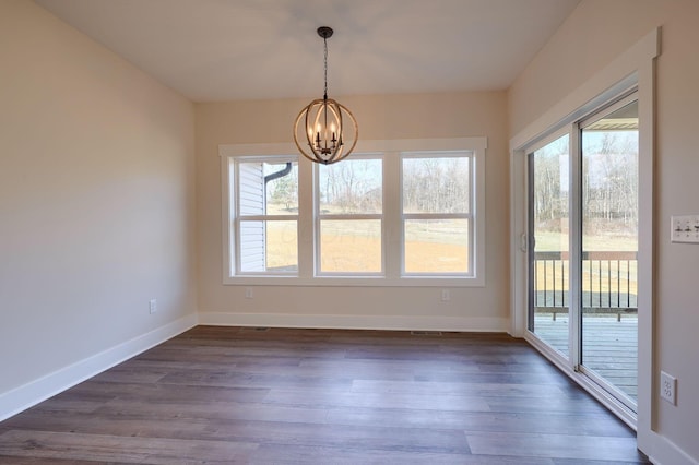 unfurnished dining area featuring baseboards, dark wood-type flooring, and an inviting chandelier