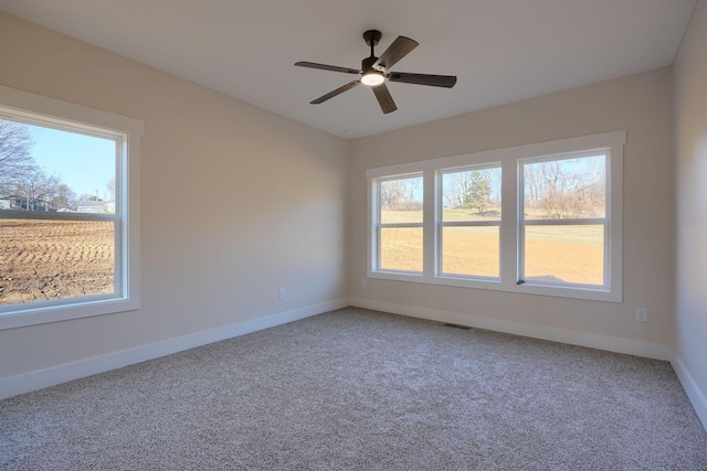 carpeted spare room with visible vents, baseboards, a healthy amount of sunlight, and ceiling fan