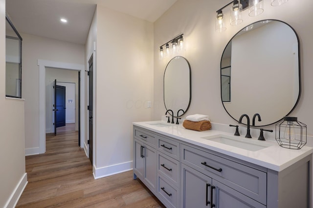 full bath featuring double vanity, wood finished floors, baseboards, and a sink