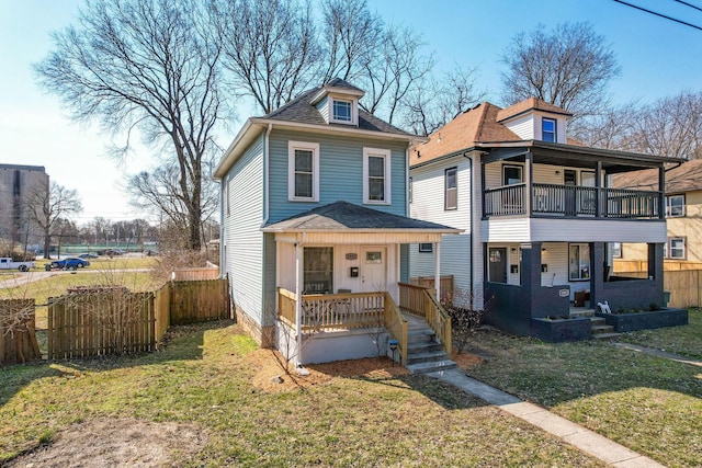 traditional style home with roof with shingles, covered porch, a front yard, and fence