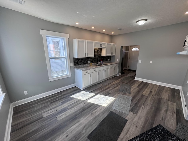 kitchen with baseboards, a sink, dark wood-type flooring, white cabinetry, and tasteful backsplash