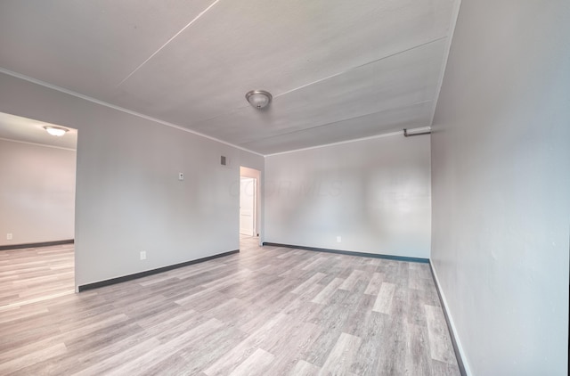 empty room featuring baseboards, light wood-type flooring, and ornamental molding