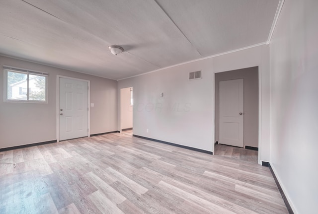 empty room featuring ornamental molding, light wood-style floors, visible vents, and baseboards