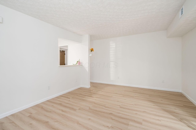 empty room with light wood-style flooring, visible vents, baseboards, and a textured ceiling