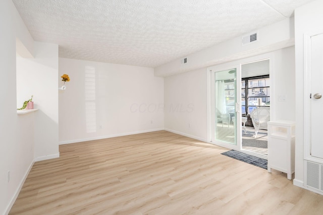 unfurnished room with light wood-type flooring, visible vents, baseboards, and a textured ceiling