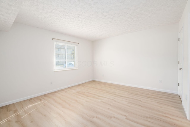 empty room with light wood-style flooring, a textured ceiling, and baseboards