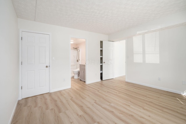 unfurnished bedroom with baseboards, light wood-style floors, ensuite bath, and a textured ceiling