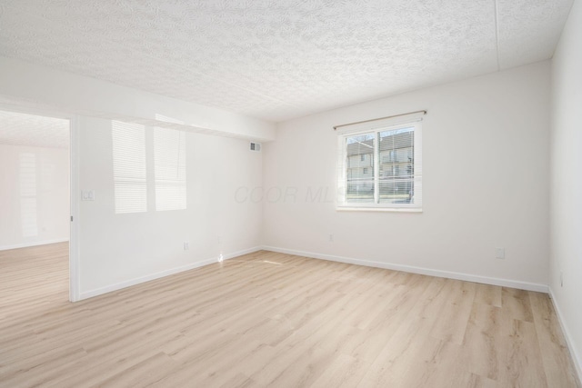 spare room with baseboards, visible vents, a textured ceiling, and light wood-style floors