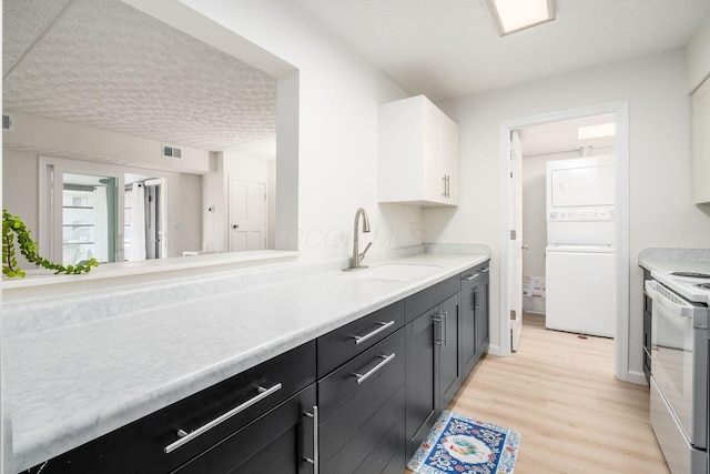 kitchen with stacked washing maching and dryer, a sink, light countertops, light wood-style floors, and white electric range