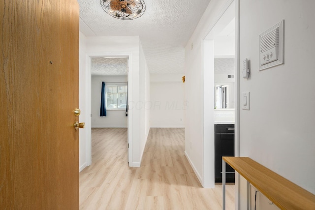 hall featuring light wood-type flooring, baseboards, and a textured ceiling