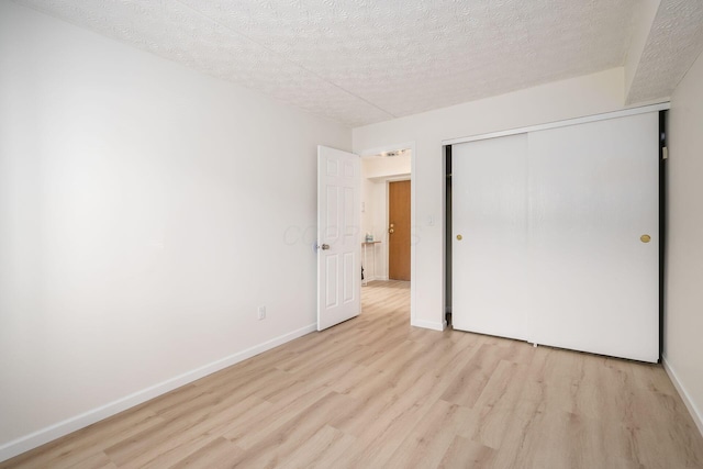 unfurnished bedroom featuring baseboards, a closet, light wood finished floors, and a textured ceiling