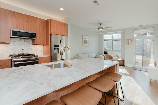 kitchen with brown cabinetry, visible vents, a sink, appliances with stainless steel finishes, and a kitchen bar