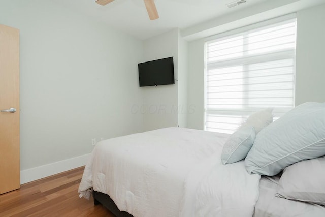 bedroom featuring ceiling fan, baseboards, multiple windows, and wood finished floors