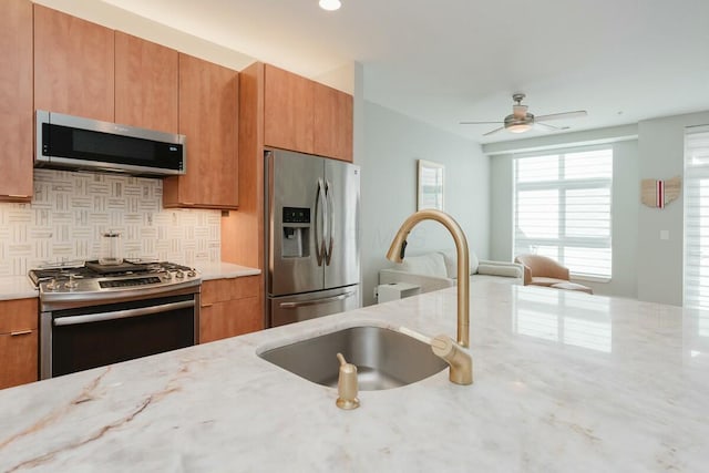 kitchen with a ceiling fan, a sink, light stone counters, tasteful backsplash, and stainless steel appliances