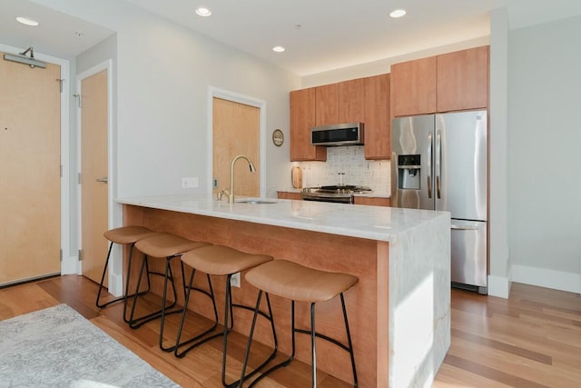 kitchen featuring a sink, appliances with stainless steel finishes, a kitchen bar, tasteful backsplash, and light wood-type flooring