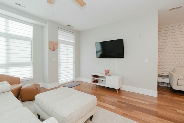 living room with ceiling fan, light wood-style floors, visible vents, and baseboards