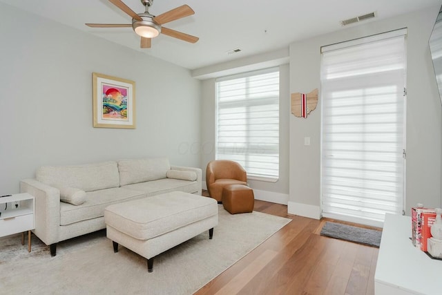 living area featuring visible vents, baseboards, light wood-style floors, and a ceiling fan