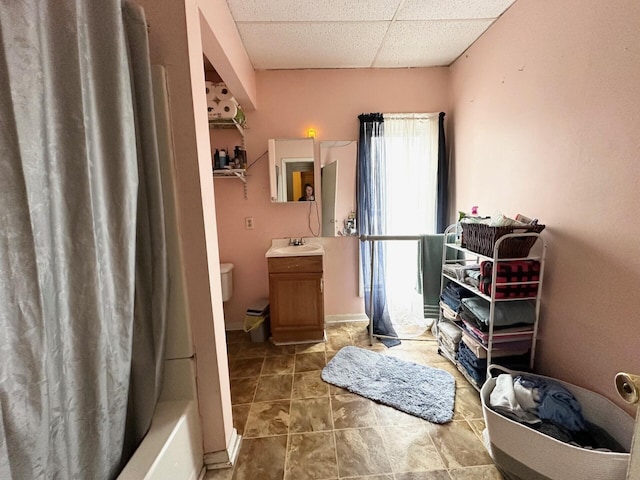 bathroom featuring a drop ceiling, shower / tub combo, toilet, and vanity