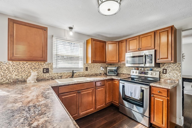 kitchen with brown cabinetry, dark wood-style flooring, appliances with stainless steel finishes, and a sink