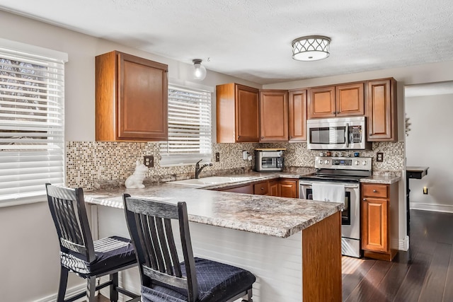 kitchen featuring a sink, stainless steel appliances, brown cabinetry, and dark wood-style flooring