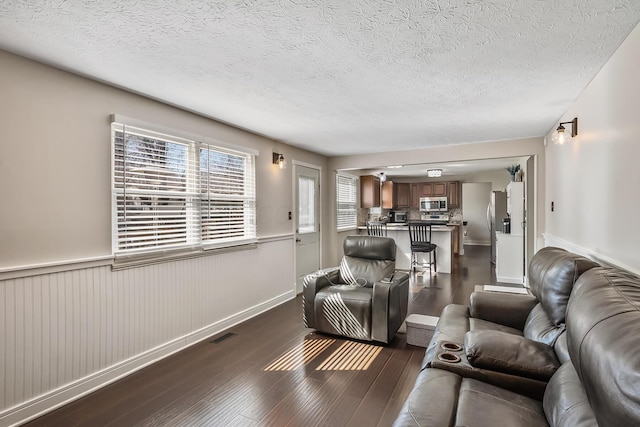 living area featuring visible vents, baseboards, a wainscoted wall, a textured ceiling, and dark wood-style flooring