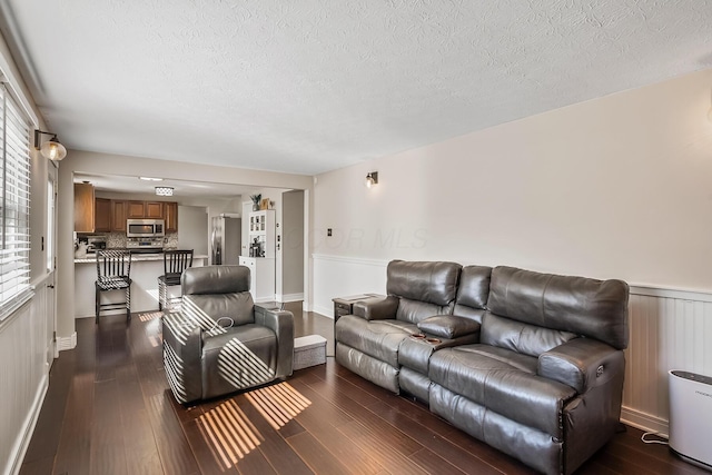 living room featuring dark wood-style floors, a wainscoted wall, and a textured ceiling