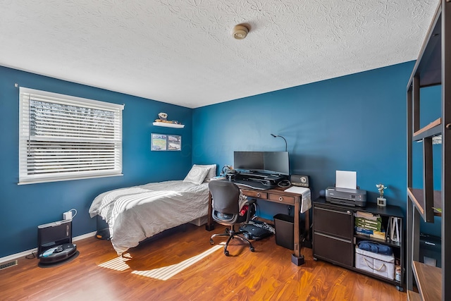 bedroom featuring visible vents, a textured ceiling, baseboards, and wood finished floors