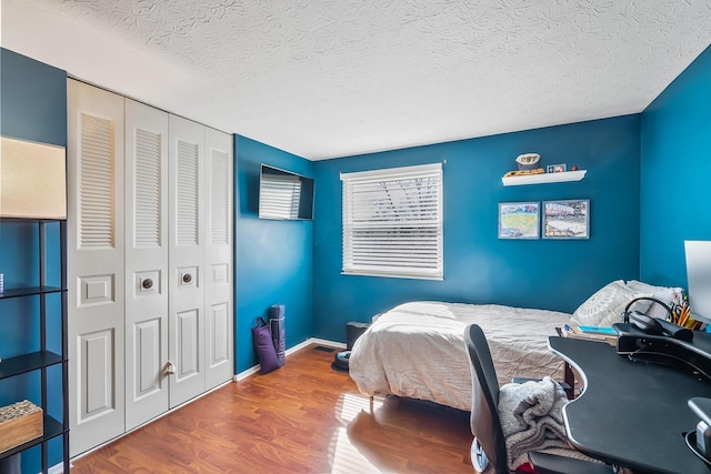 bedroom with a closet, a textured ceiling, baseboards, and wood finished floors