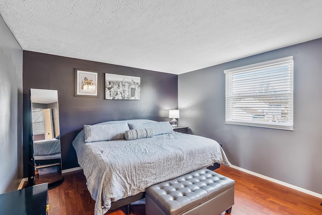 bedroom featuring baseboards, a textured ceiling, and wood finished floors