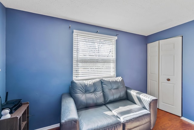 living area featuring a textured ceiling, baseboards, and wood finished floors