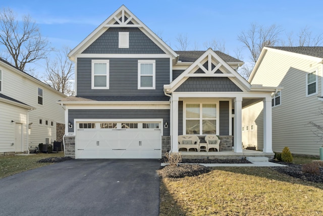 craftsman house with stone siding, an attached garage, covered porch, and driveway