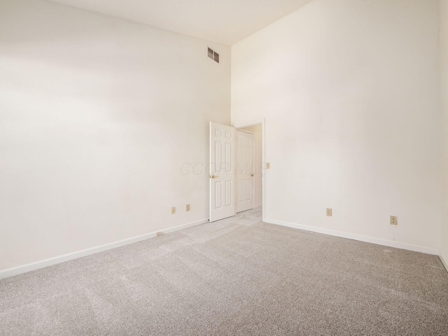 empty room featuring light carpet, visible vents, a high ceiling, and baseboards