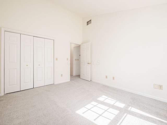 unfurnished bedroom featuring baseboards, visible vents, carpet floors, high vaulted ceiling, and a closet