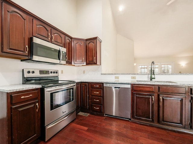 kitchen with dark wood-type flooring, dark brown cabinetry, a peninsula, stainless steel appliances, and a sink