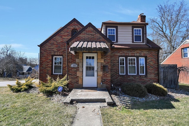 bungalow with a front yard, fence, a standing seam roof, a chimney, and brick siding