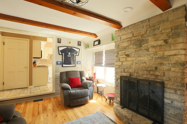 living area featuring beam ceiling, a stone fireplace, visible vents, and wood finished floors