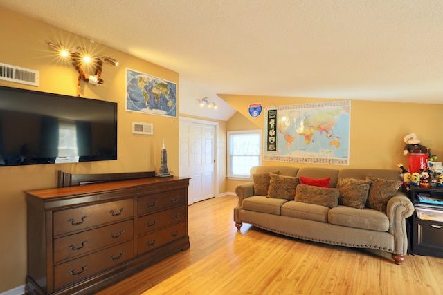 living area featuring vaulted ceiling, visible vents, light wood finished floors, and a textured ceiling